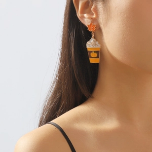 Detailopname van herfst oorbellen met oranje esdoornblad en koffiekopje met pompoen ontwerp
