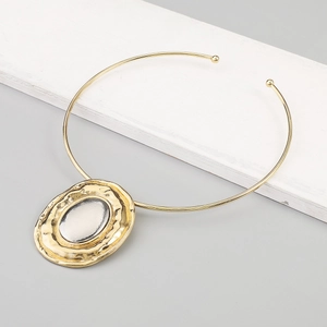 Close-up of golden collar necklace with large oval dual-tone hammered metal pendant
