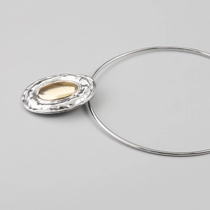 Detail of minimalist mixed-metal oval pendant with silver hammered texture and gold mirror finish