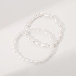 Detailed view of layered baroque and rice-shaped pearl bracelets on white background