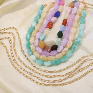 Details bunter Harzperlen-Lagen und goldener Ketten-Choker auf Seidenhintergrund