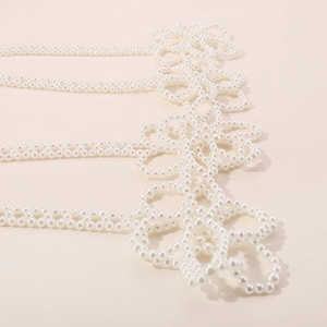 Détail d'une chaîne de corps en perles blanches avec des motifs floraux perlés complexes