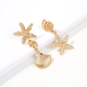 Détail de boucles d'oreilles étoiles de mer et coquillages dorés sur un support blanc
