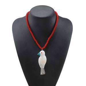 Dettaglio della collana di perle rosse con ciondolo uccello in resina su busto nero