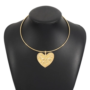 Gros plan du collier doré avec pendentif cœur orné d'un motif de visage tribal en relief