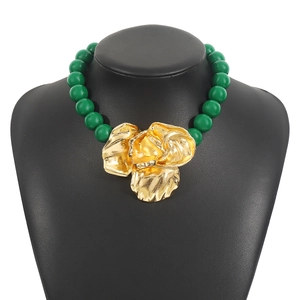 Close-up of a green beaded necklace with a large golden floral pendant on a black bust