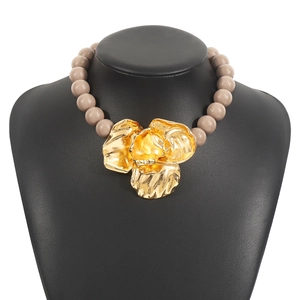 Detailed macro of oversized gold metal floral pendant on light brown beaded necklace