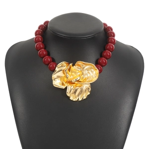 Detail of deep red beaded necklace featuring a large vintage style golden flower pendant