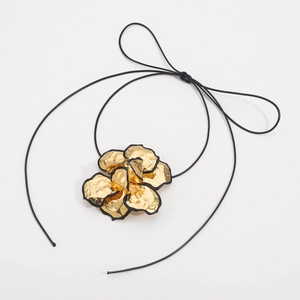 Detail van een 3D gouden bloem hanger met zwarte randen aan een minimalistisch koord
