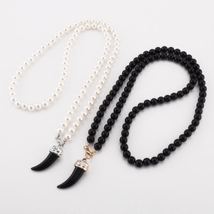 Detail of beaded necklace featuring white pearl, black beads, and wolf tooth pendants
