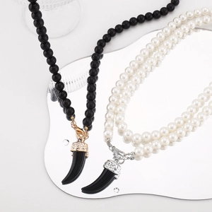 Macro detail of bead necklace with wolf tooth pendant on a reflective mirror surface