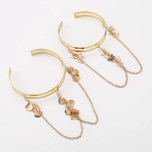 Detail view of gold arm cuffs featuring delicate butterfly and shell charms with chain fringe