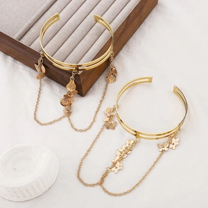 Detail view of gold open arm cuffs with butterfly and shell charms on delicate chains