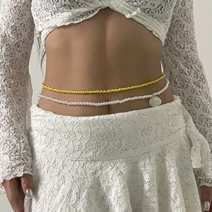 Detalle de cadenas de cintura con cuentas amarillas, perlas falsas y colgante de caracola