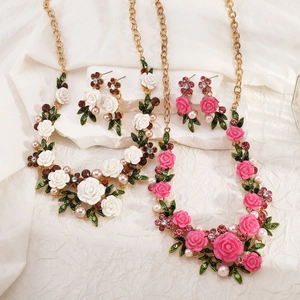 Detalle de conjuntos de collar y pendientes de flores esmaltadas con perlas blancas