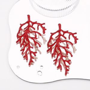 Macro detail of red coral branch earrings with gold glitter accents on a mirror