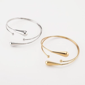 Détail de bracelets de bras géométriques or et argent avec pendentifs goutte d'eau