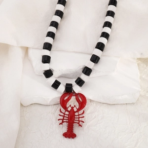 Detail van kralenketting met een felrode kreeft hanger op een witte stenen dienblad
