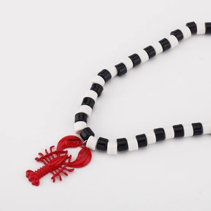 Detail van een rode kreeft hanger aan een zwart-witte kralen ketting voor dames