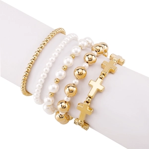 Detail of four-piece gold beaded bracelet set with cross charms on a white display