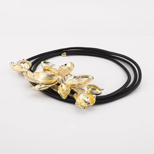 Detailed macro view of an oversized gold flower buckle on multi-strand black cord belt