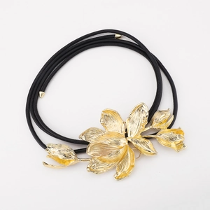 Detailed macro view of a large golden tulip floral buckle on a black slim cord belt