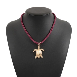 Dettaglio del ciondolo tartaruga dorata su cordino intrecciato bordeaux per collana marina