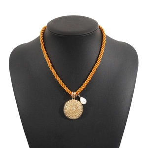 Dettaglio di un ciondolo tondo dorato con perla su una collana in corda intrecciata arancione