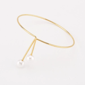 Primer plano detallado de un brazalete dorado minimalista con dos perlas blancas
