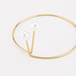 Vista detallada del brazalete dorado minimalista con dos elegantes perlas blancas