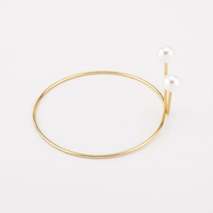Detalle macro de la pulsera de brazalete de metal dorado con elegantes perlas dobles