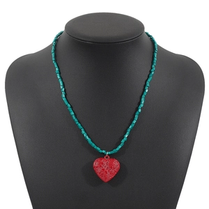 Dettaglio collana boho con perline verde acqua e ciondolo a cuore rosso su manichino