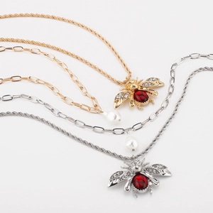 Detail view of gold chunky chain necklace with red gemstone bee pendant and baroque pearl