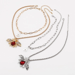 Detailed view of layered bee necklace with red gemstone and drop pearl pendant