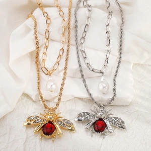 Detail of layered gold and silver chains featuring a crystal bee pendant and pearl