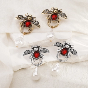 Macro detail of bee earrings with red gemstones and hanging teardrop pearls on stone