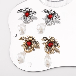Macro detail of bee earrings with red beads, crystal wings and teardrop pearls