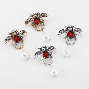 Macro detail of bee-shaped pendants with red stones, rhinestones and faux pearls