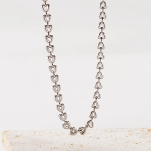 Détail d'un collier à maillons en forme de cœur argenté sur un support en pierre