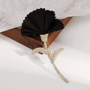 Close-up of black fabric flower brooch with gold-toned sparkling crystal leaves and stem