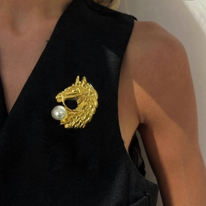 Elegant gold horse head brooch with pearl detail pinned on a formal black suit vest