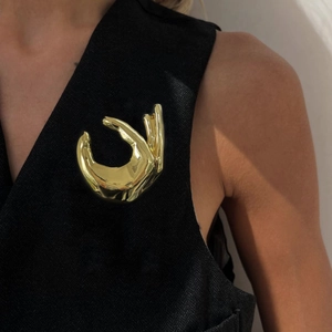 Elegant golden hand-shaped brooch in polished metal, worn on black textured clothing