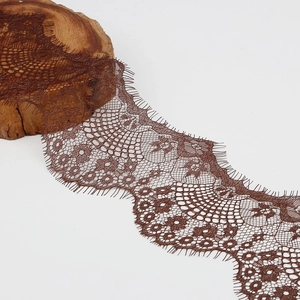 Detailed close-up of dark brown eyelash lace fabric with floral embroidery on wooden block