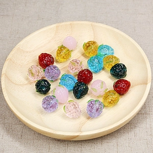 Colorful handmade glass strawberry charms for DIY jewelry making on wooden plate