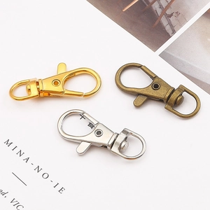 Trois mousquetons porte-clés en finitions or, bronze et argent sur un fond blanc