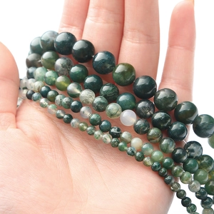 Macro shot of natural green moss agate beads in various sizes on palm for size comparison