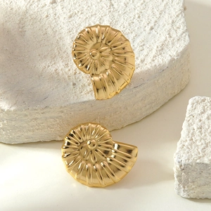 Detailansicht goldener Spiral-Ohrringe im Nautilus-Design auf weißen Natursteinen