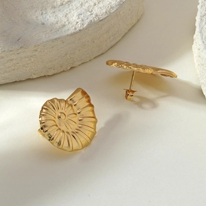 Makroaufnahme goldener Nautilus-Ohrstecker auf strukturiertem weißem Steinuntergrund