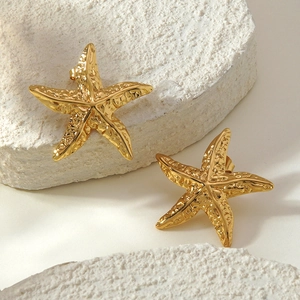 Strukturierte goldene Seestern-Ohrringe aus Edelstahl auf weißem Stein für den Strand