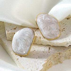 Détail de boucles d'oreilles dorées avec incrustation de marbre sur tissu de soie